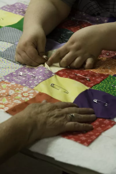 To prevent the quilt top, batting, and backing from shifting during the final stitching process, Reta Smith and her student feed safety pins through each square of fabric at the Knott County, KY Common Threads: Quilting class in 2019. Photo Credit: Jackson Hall 