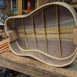 An open guitar body that has not yet been assembled resting on a worktable.