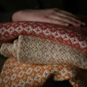 A hand resting on three folded woven blankets.